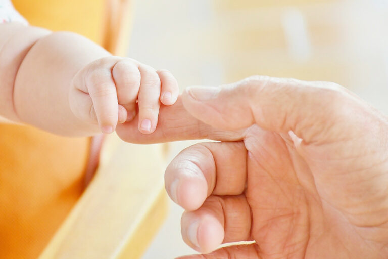 Die Hand eines Babys liegt auf dem Zeigefinger eines Erwachsenen