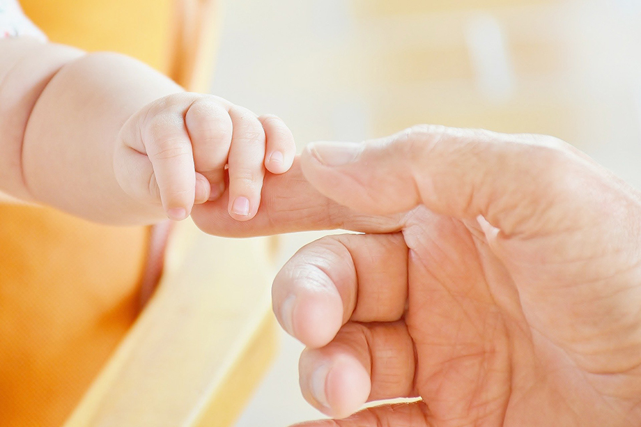 Die Hand eines Babys liegt auf dem Zeigefinger eines Erwachsenen