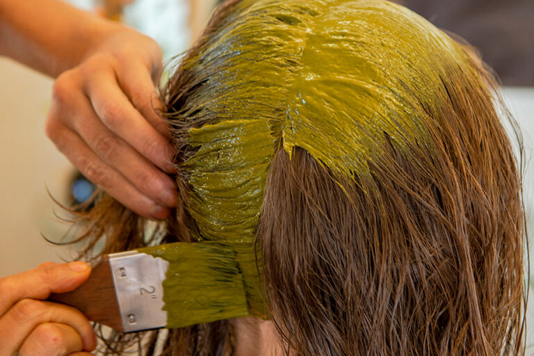 Eine gelb-braune Farbe wird mit einem Pinsel auf das Haar einer Frau aufgetragen