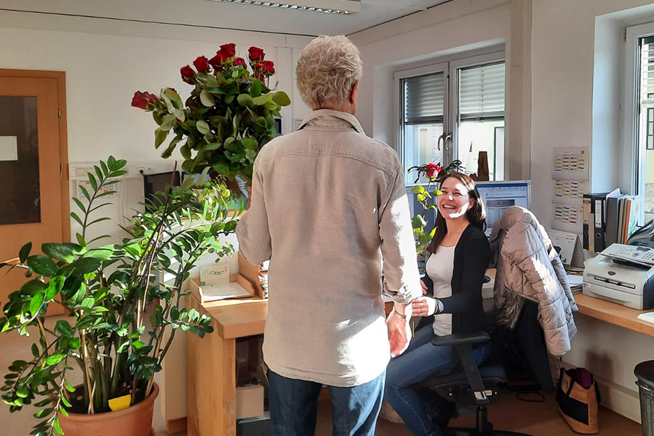 Ein Mann überreicht einer jungen Frau an ihrem Schreibtisch eine rote Rose