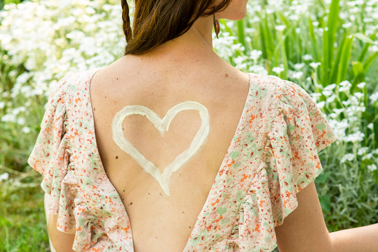Rücken einer jungen Frau mit einem Herzen aus Sonnencreme