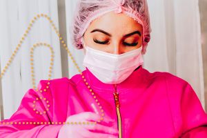 Eine Frau in einem rosafarbenen Schutzanzug und Mund-Nasen-Schutz hantiert mit Chemikalien