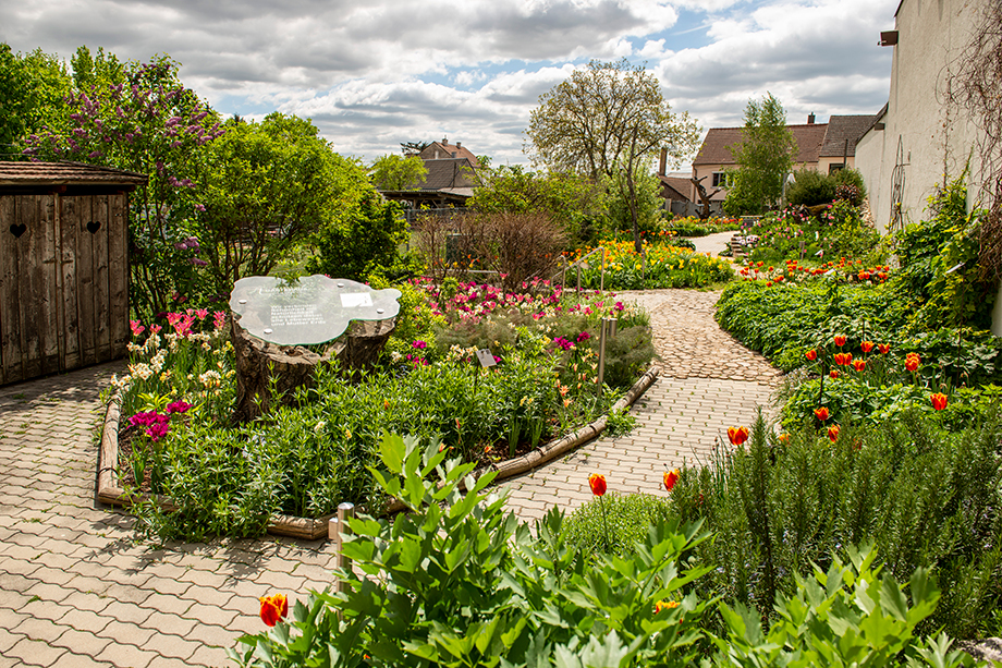 Prachtvoller Garten mit viel Grün und bunten Blumen, der sich um Wege aus Stein schlingt