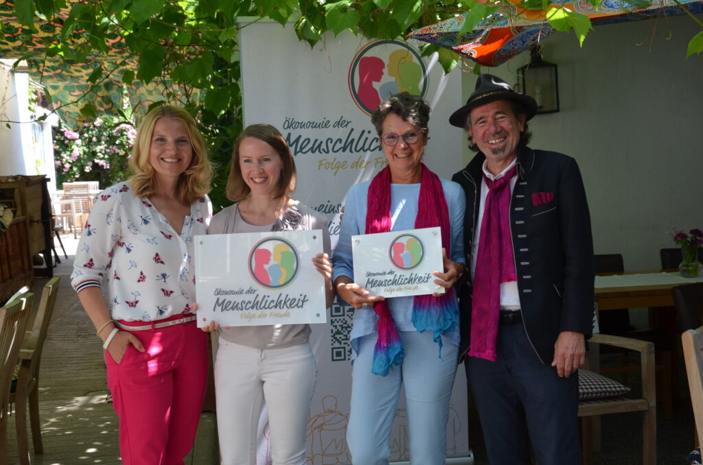 Drei Frauen und ein Mann halten das Logo der "Ökonomie der Menschlichkeit"