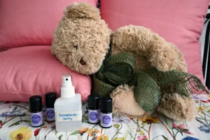 Teddybär liegt auf Polster, vorne stehen eine kleine Flasche und ätherische Öle