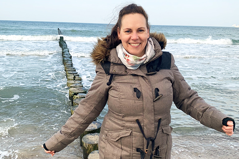 Eine Frau mittleren Alters steht mit winterlicher Bekleidung vor dem Meer