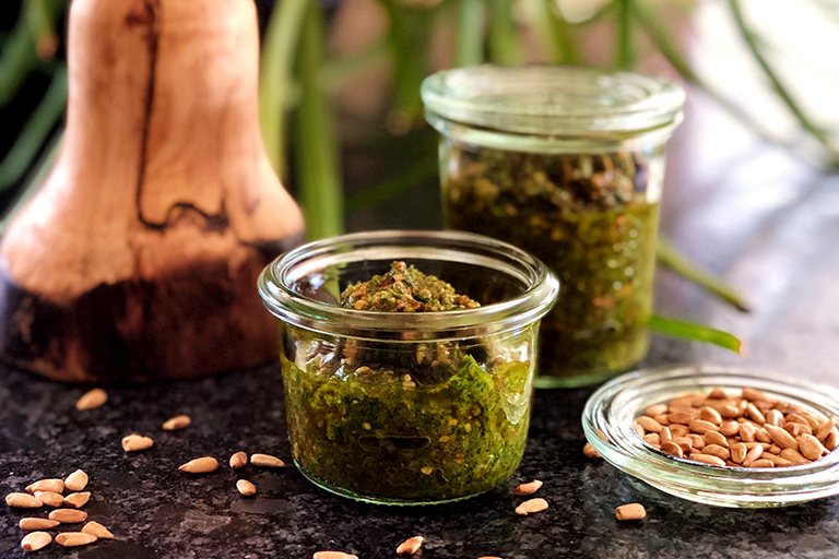 Grünes Löwenzahnpesto in zwei Gläsern mit Sonnenblumenkernen rundherum