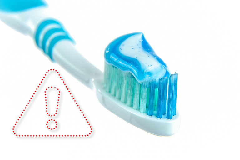 Blau glitzernde Zahnpasta auf einer blauen Zahnbürste, daneben ein Rufzeichen