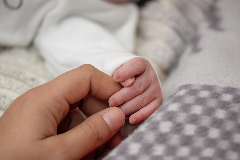 Ein Baby berührt mit seinen Fingern die Hand seiner Mutter