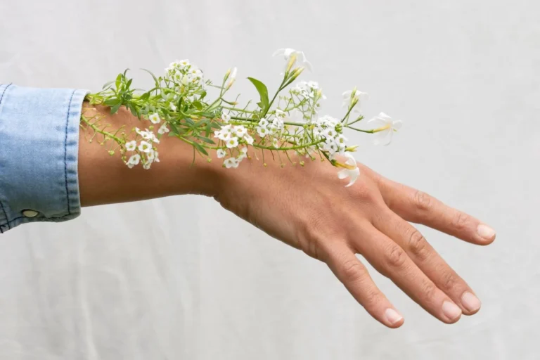 Redewendungen Haut: Hand mit weißen Blumen als Symbol für sensible, berührbare Haut und deren Bedeutung.