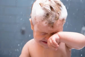 Weinendes Kleinkind mit brennendem Shampoo-Schaum in den Augen; verdeutlicht die Reizung durch synthetische Tenside und Duftstoffe.