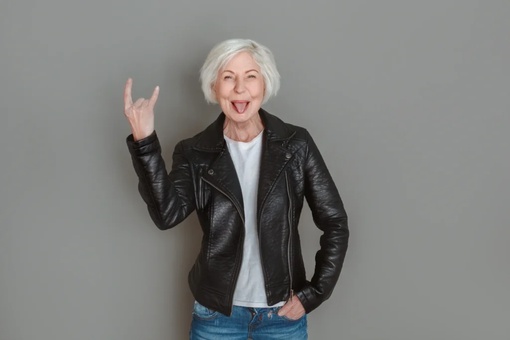 Selbstbewusste ältere Frau mit weißem Haar und Lederjacke lächelt in die Kamera – Symbol für Happy Aging und selbstbestimmtes Älterwerden.