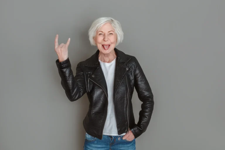 Selbstbewusste ältere Frau mit weißem Haar und Lederjacke lächelt in die Kamera – Symbol für Happy Aging und selbstbestimmtes Älterwerden.